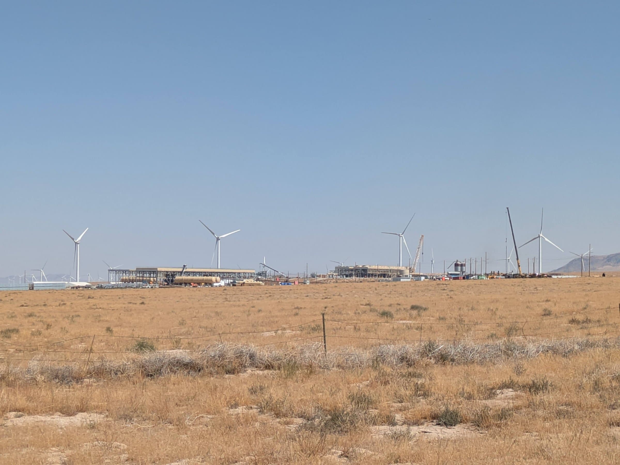 Fervo Energy's Cape Station geothermal plant under construction in Beaver County, Utah, with wind turbines on the horizon